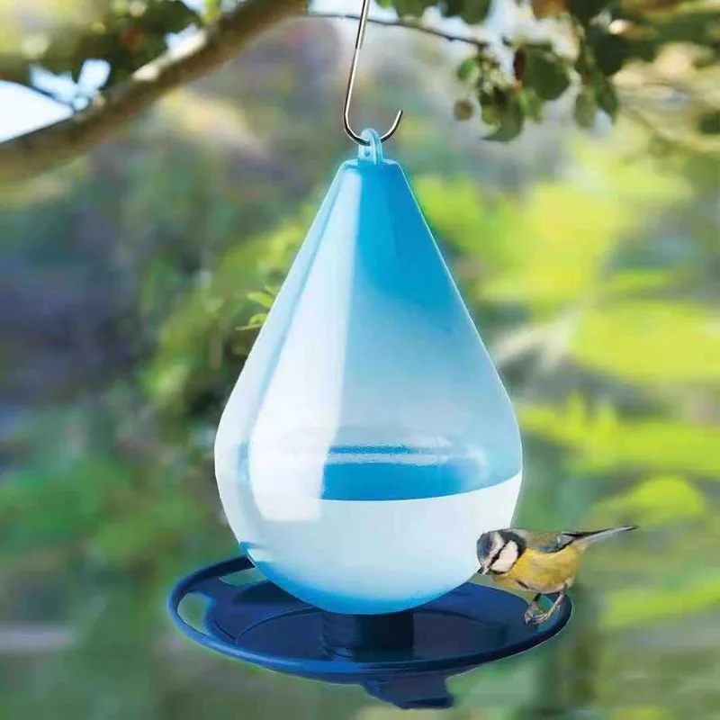 Blue teardrop bird feeder hanging in a garden with a bird on the tray