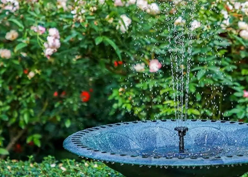 Solar fountain spraying in a blue bird bath among roses