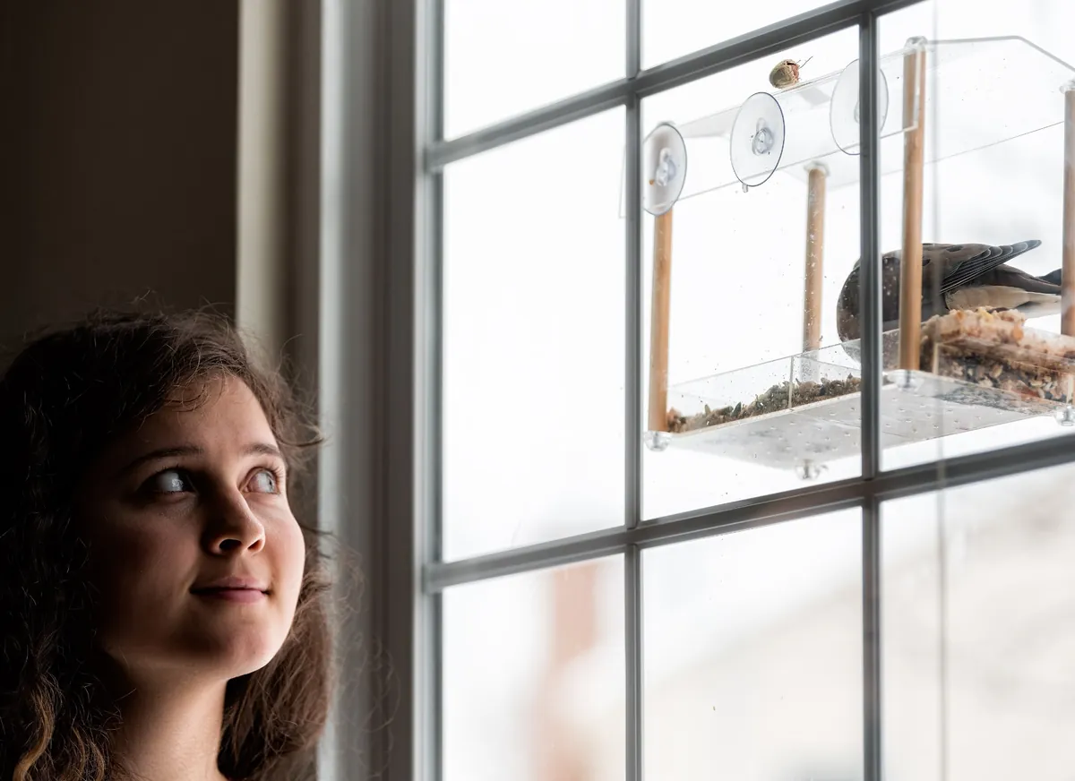 A woman smiles at a mourning dove feeding at a clear window feeder fixed to her window