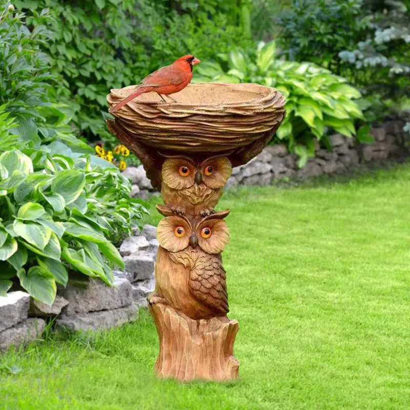 Owl pedestal bird bath in a garden bed with a bird on the dish